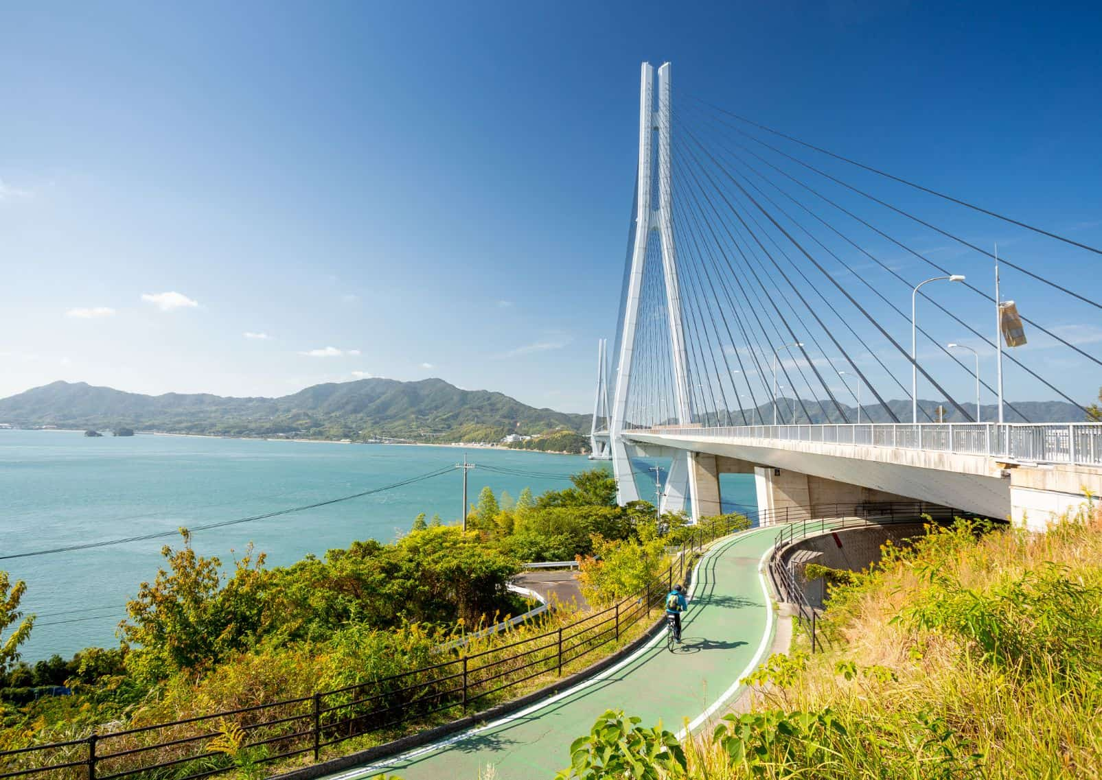 Een fietser legt de Shimanami Kaido-route af met op de achtergrond een enorme brug en de Japanse Binnenzee.