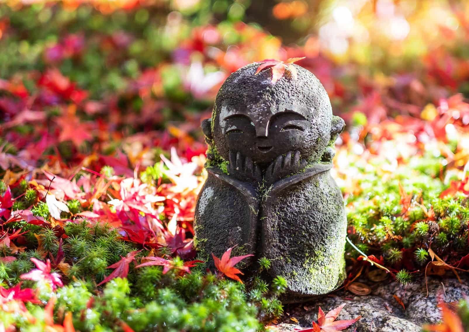 Japans Jizo-beeldje met gevallen rode esdoornbladeren in de Japanse tuin van de Enkoji-tempel, Kyoto, Japan.