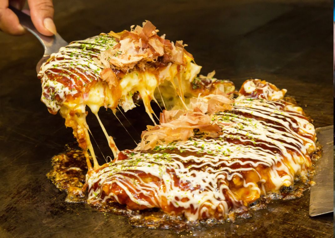 Okonomiyaki: een hartige Japanse pannenkoek met groenten, vlees of zeevruchten, rijkelijk afgedekt met mayo en bonito vlokken