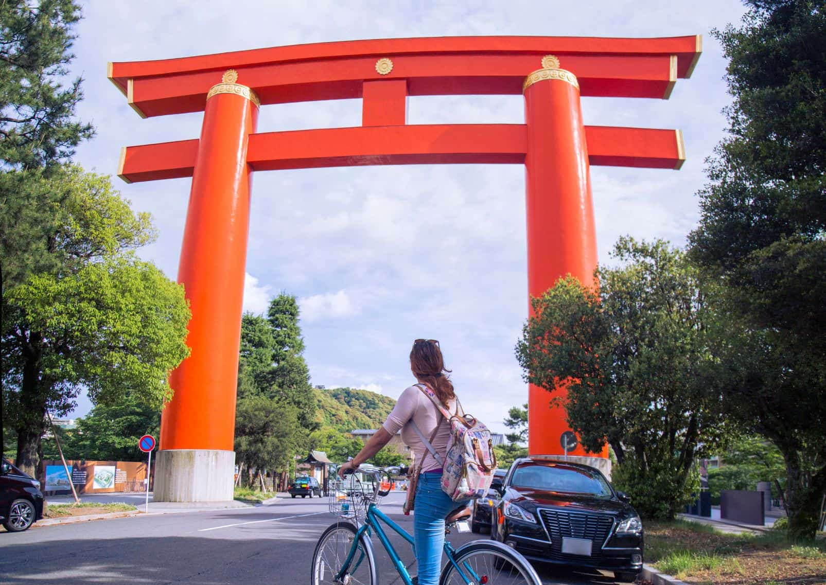 Jonge vrouw stopt met haar fiets voor een reusachtige torii in Kyoto.