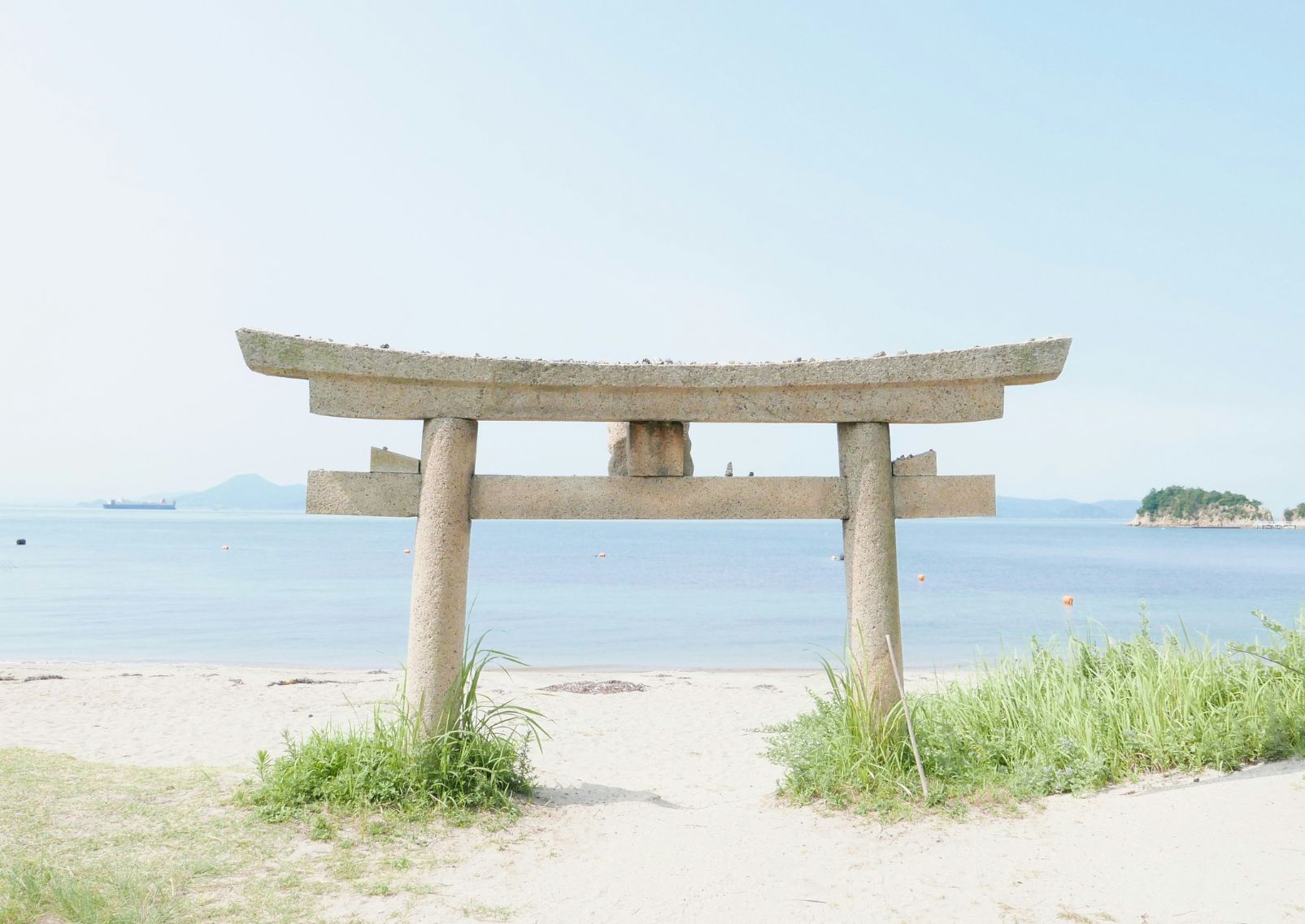  Een stenen torii poort half verzonken in het zand met de zee op de achtergrond.