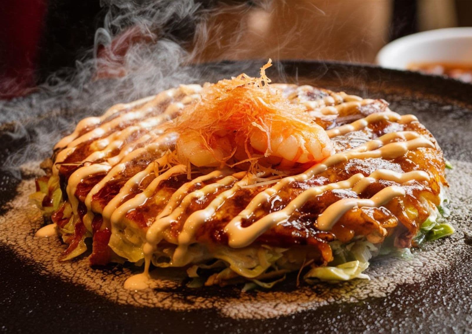 Japanse okonomiyaki wordt ter plekke bereid op een hete ijzeren bakplaat