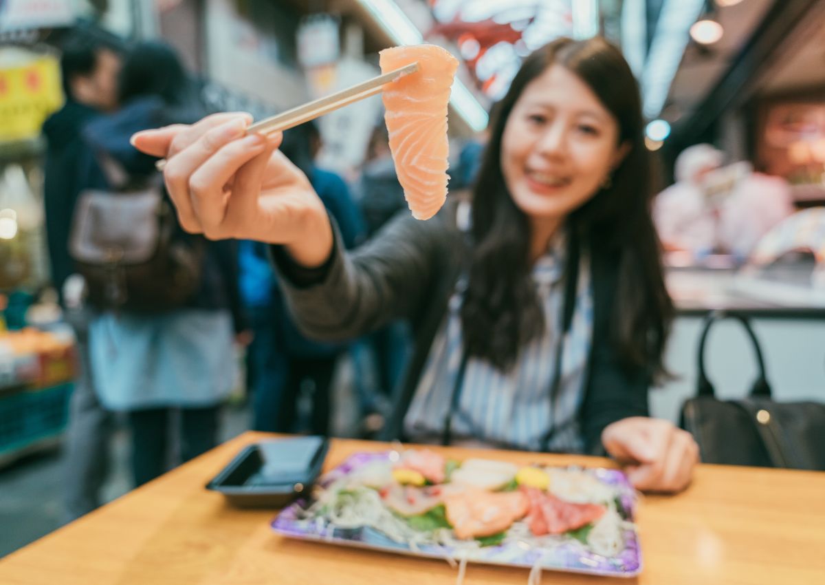 Meisje eet sushi op Kuromon Markt, Osaka, Japan an