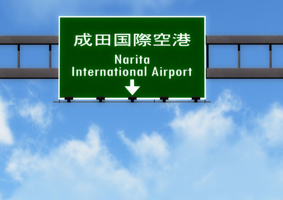 Bord naar Narita International Airport op een snelweg met een blauwe lucht als achtergrond.