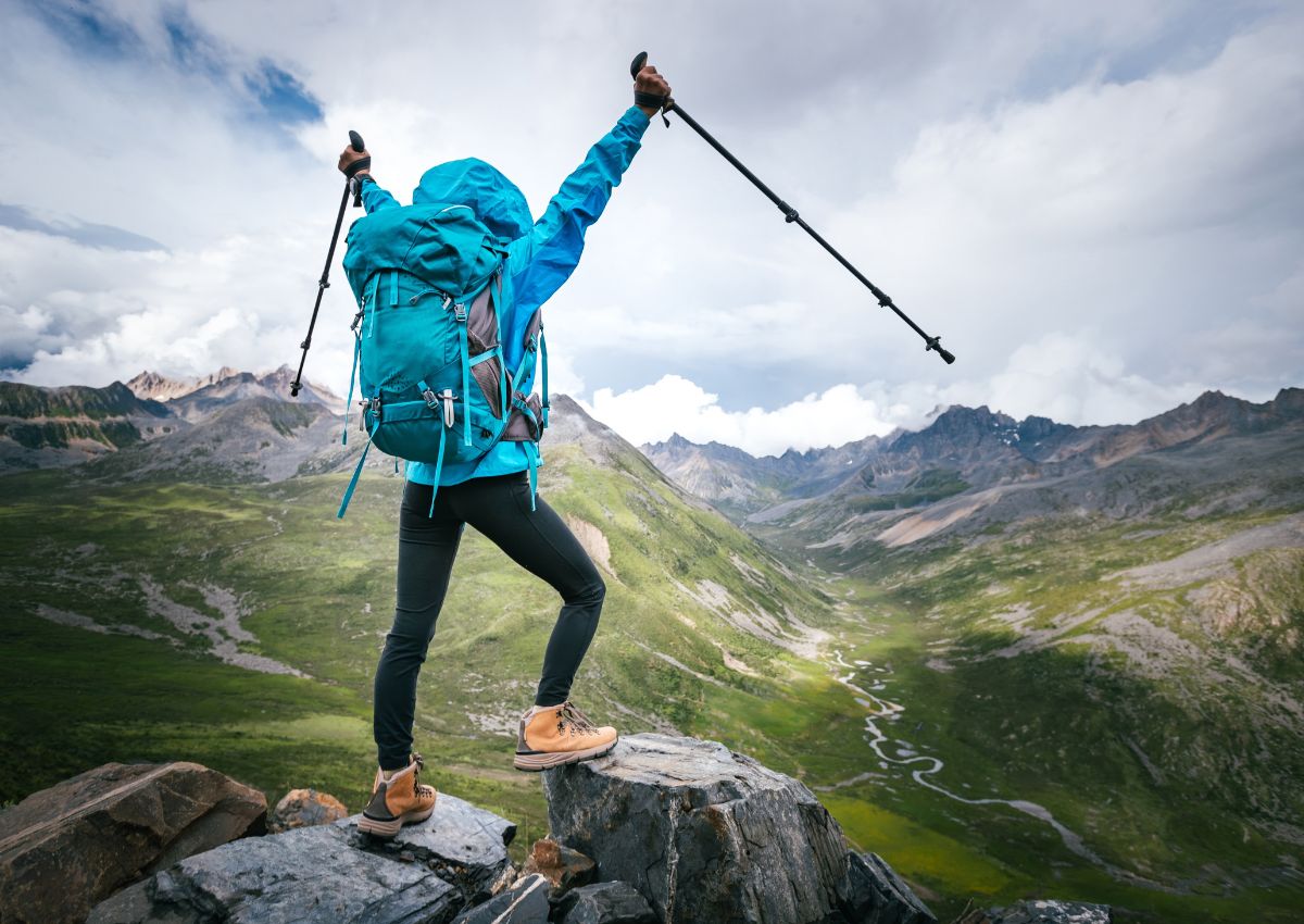 Vrouw met rugzak en wandelstokken op de top van een hooggelegen berg