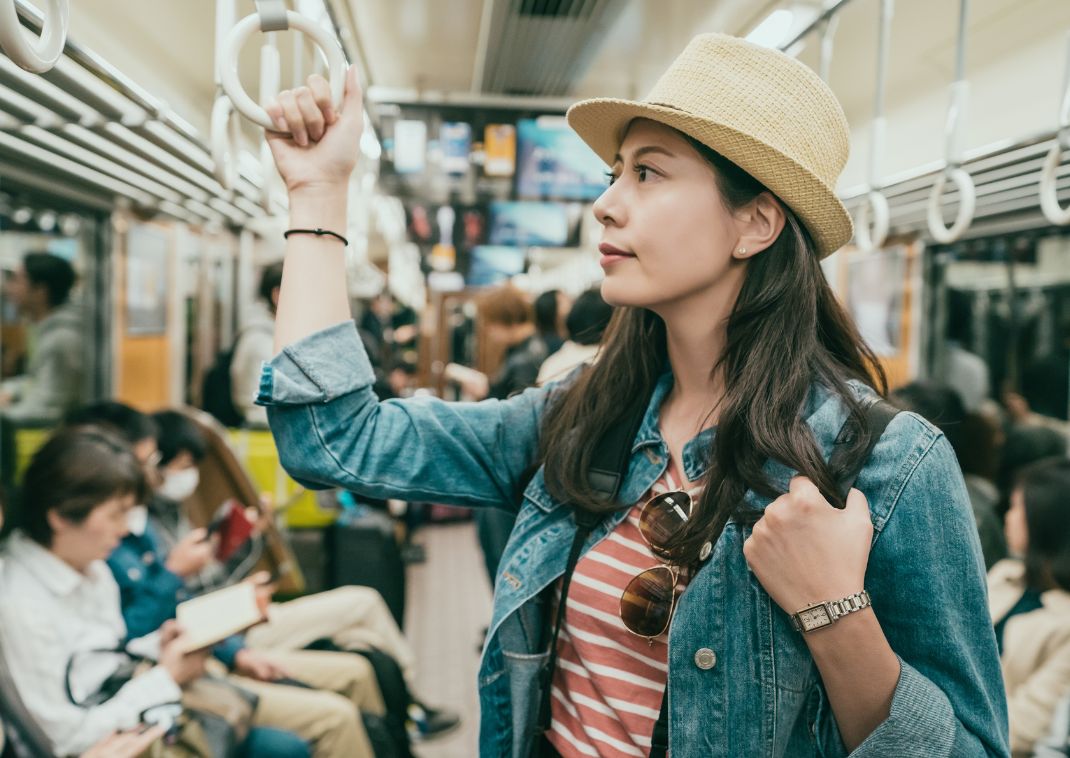 Jonge vrouwelijke Aziatische reiziger houdt zich vast terwijl ze in een Japanse metro staat.