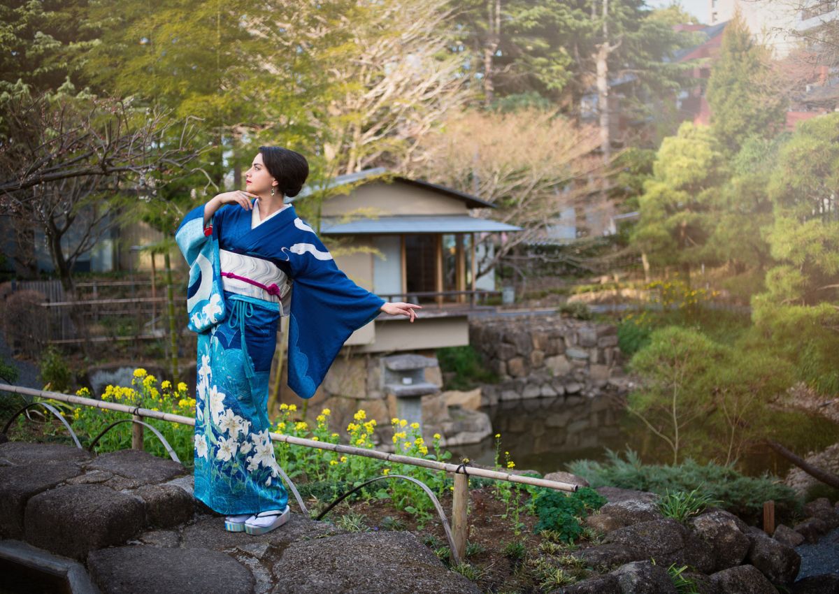 Vrouw in een blauwe houmongi-kimono poseert in een Japanse theetuin