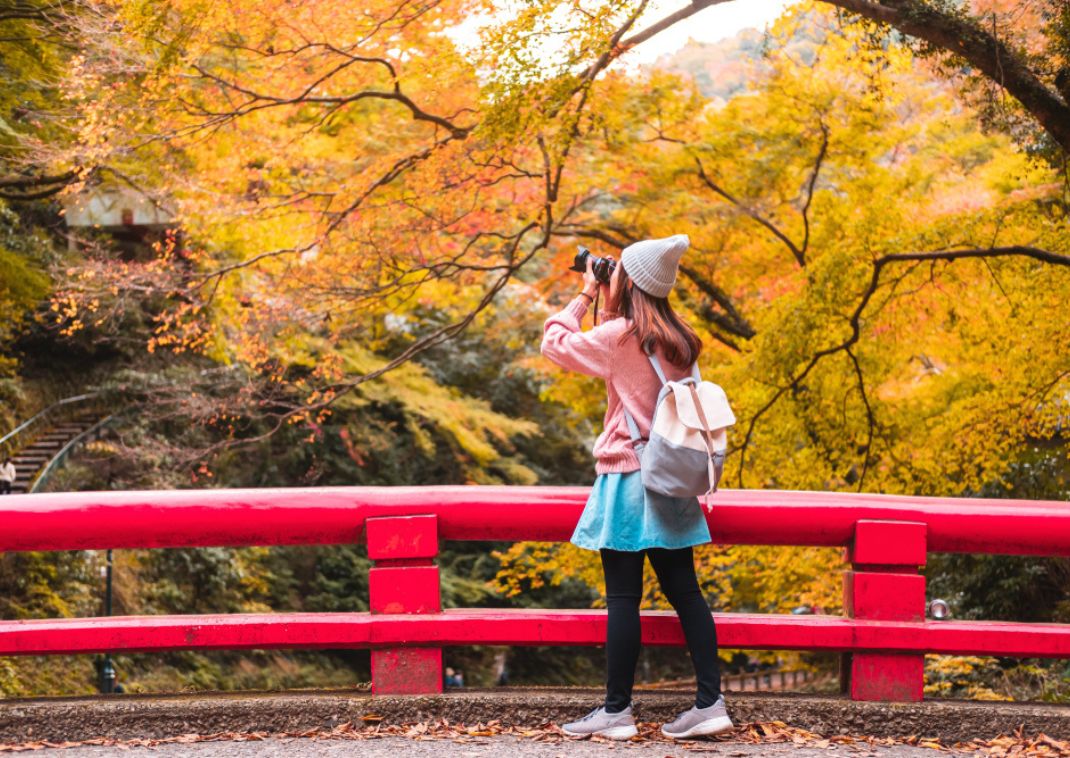 Jonge vrouwelijke reiziger fotografeert een prachtig herfstlandschap in Japan