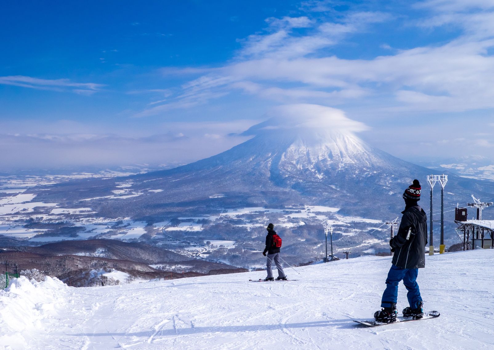 Snowboarder en skiër kijken naar de met sneeuw bedekte vulkaan met wolkenkap (Niseko, Hokkaido, Japan).