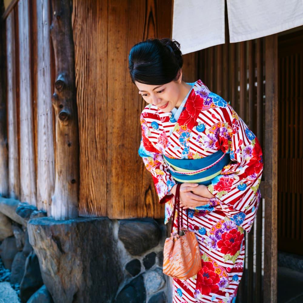 Japanse vrouw in een kleurrijke kimono buigt voor een traditioneel houten gebouw in Kyoto