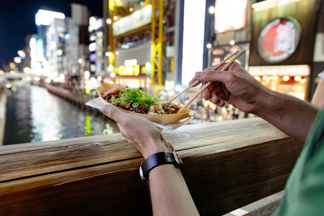 Een toerist geniet van een Takoyaki bij het Dotonbori-kanaal in Osaka, Japan