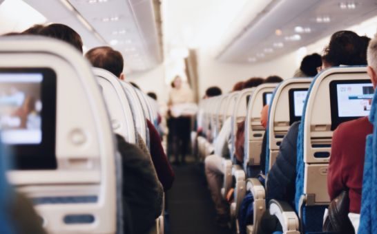 Interieur van een groot passagiersvliegtuig met zittende mensen en een stewardess in uniform die door het gangpad loopt