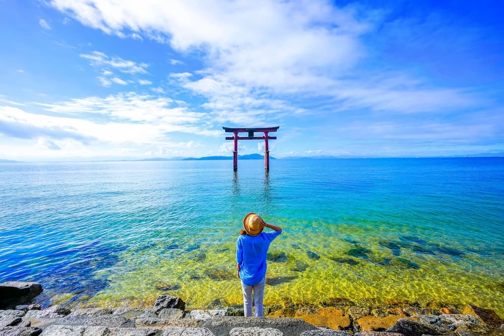 Reiziger staat bij een torii poort bij het Biwa meer in de prefectuur Shiga, Japan