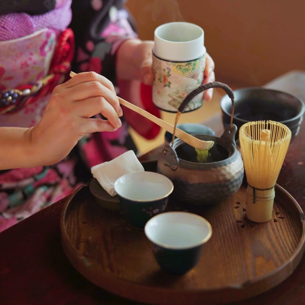 Japanse vrouw bereidt matcha thee in een traditionele theeceremonie thuis, met matcha poeder, kruiden en een theepot
