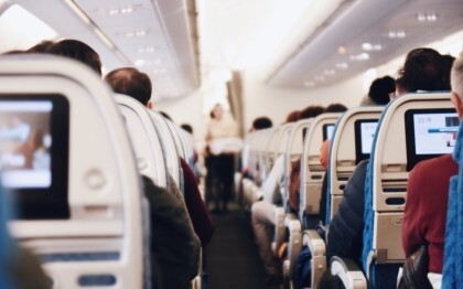 Interieur van een groot passagiersvliegtuig met zittende mensen en een stewardess in uniform die door het gangpad loopt