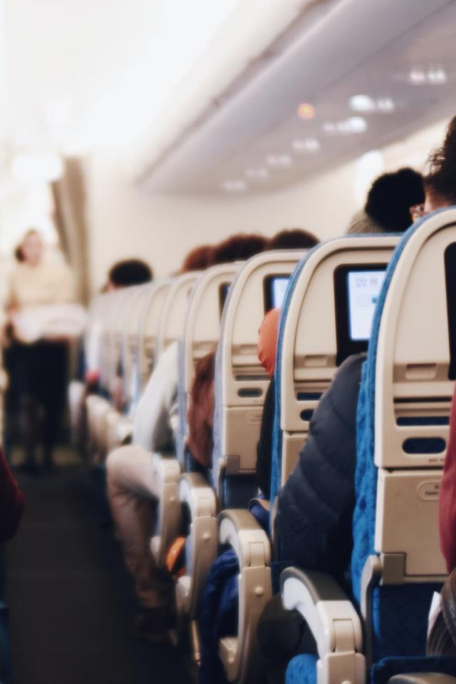 Interieur van een groot passagiersvliegtuig met zittende mensen en een stewardess in uniform die door het gangpad loopt